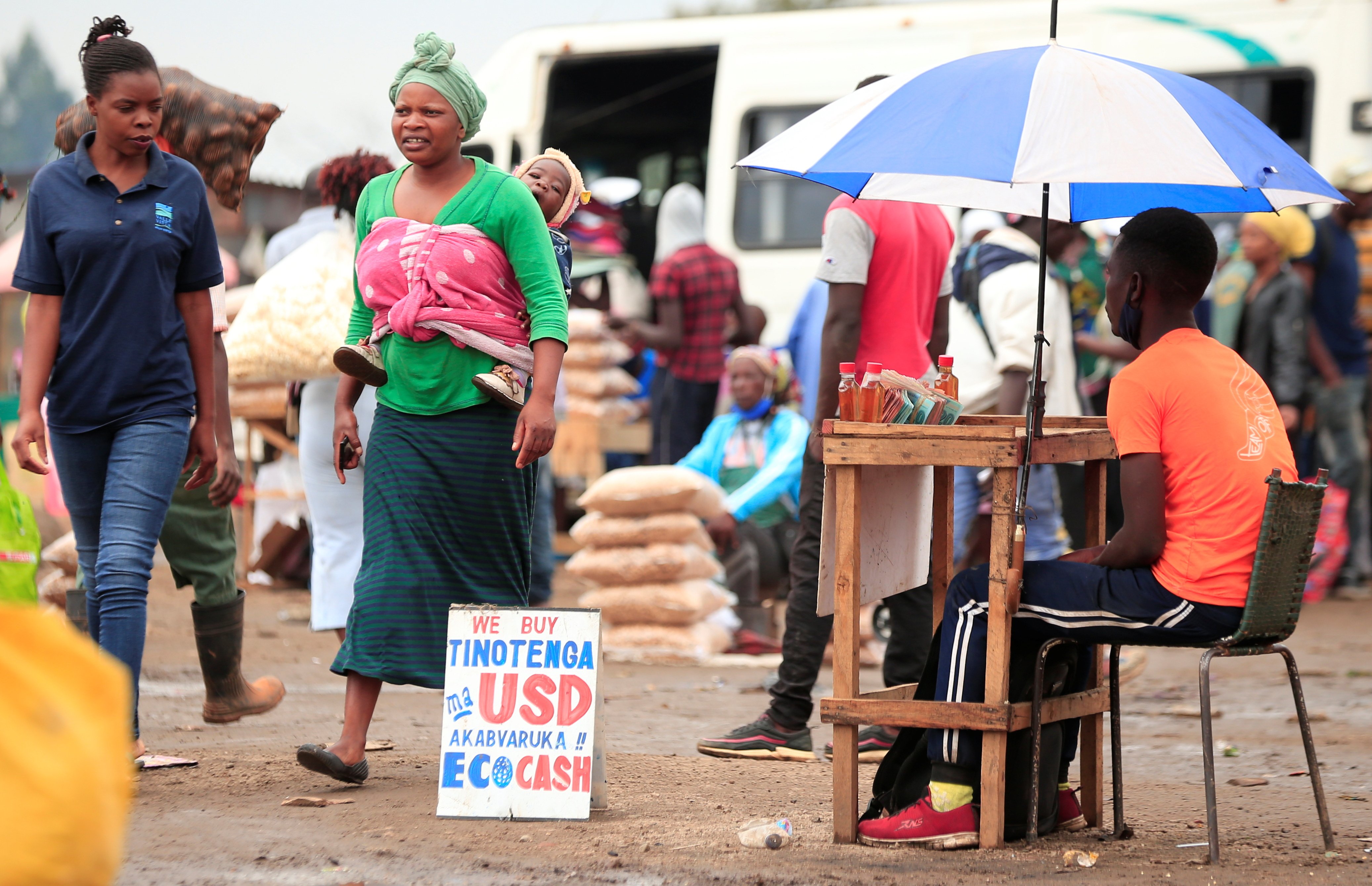 People walk past a money-changers sign at a market in Harare