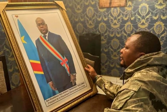 Gecko Beia in front of a photograph of President Félix Tshisekedi, March 2023.